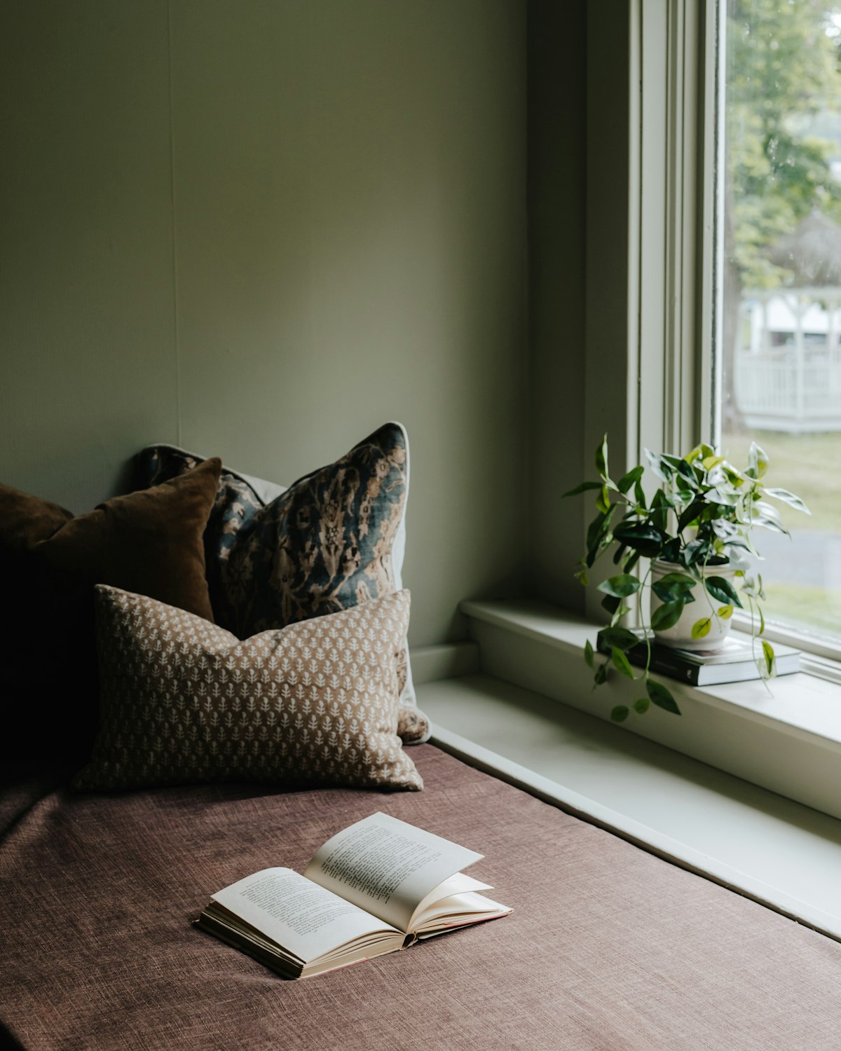 An open book on a window seat beside cushions